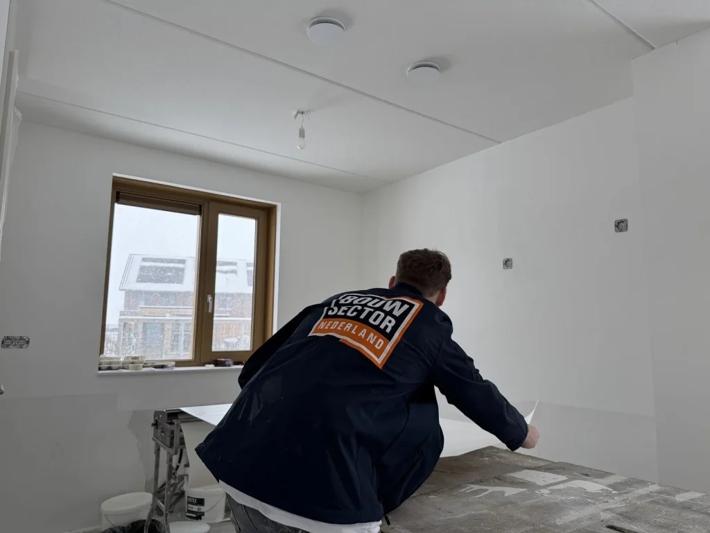 Behanger van Bouwsector Nederland in donkerblauwe werkjas pakt een baan behang van de plaktafel