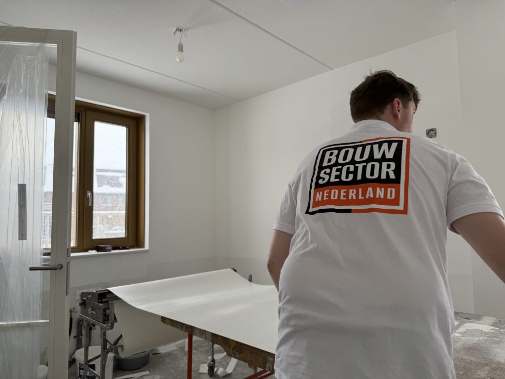 Behanger in wit shirt met het logo van Bouwsector Nederland rolt een baan uit op de plaktafel