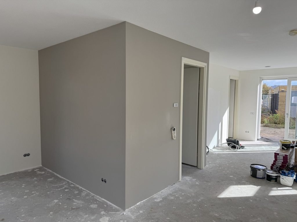 Nieuwbouwwoning met een pas gesausde grijze wand rond de hal en verfemmers op de vloer