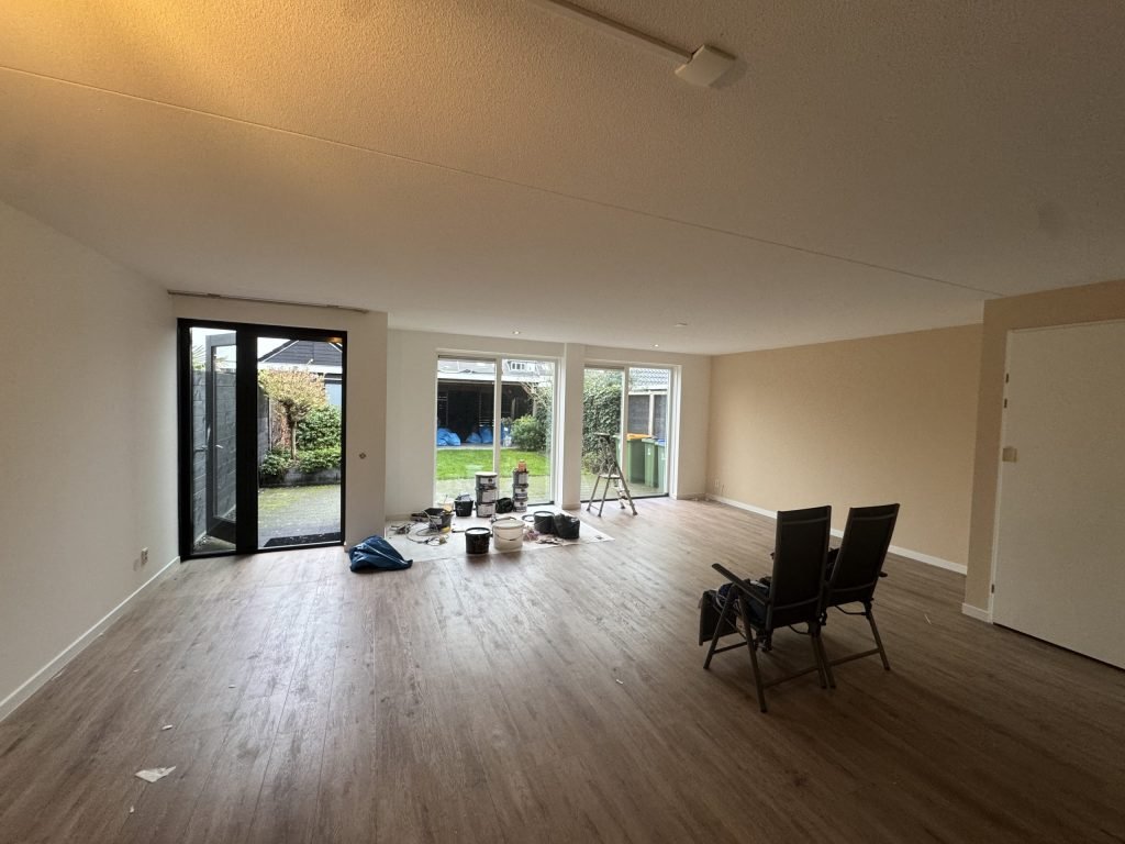 Ruime woonkamer van een bestaande woning met lichte wanden, een houten vloer en tuindeuren