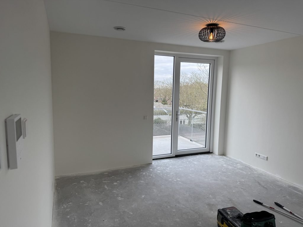 Lege nieuwbouwkamer met gladde witte wanden en een balkondeur, kort na de oplevering